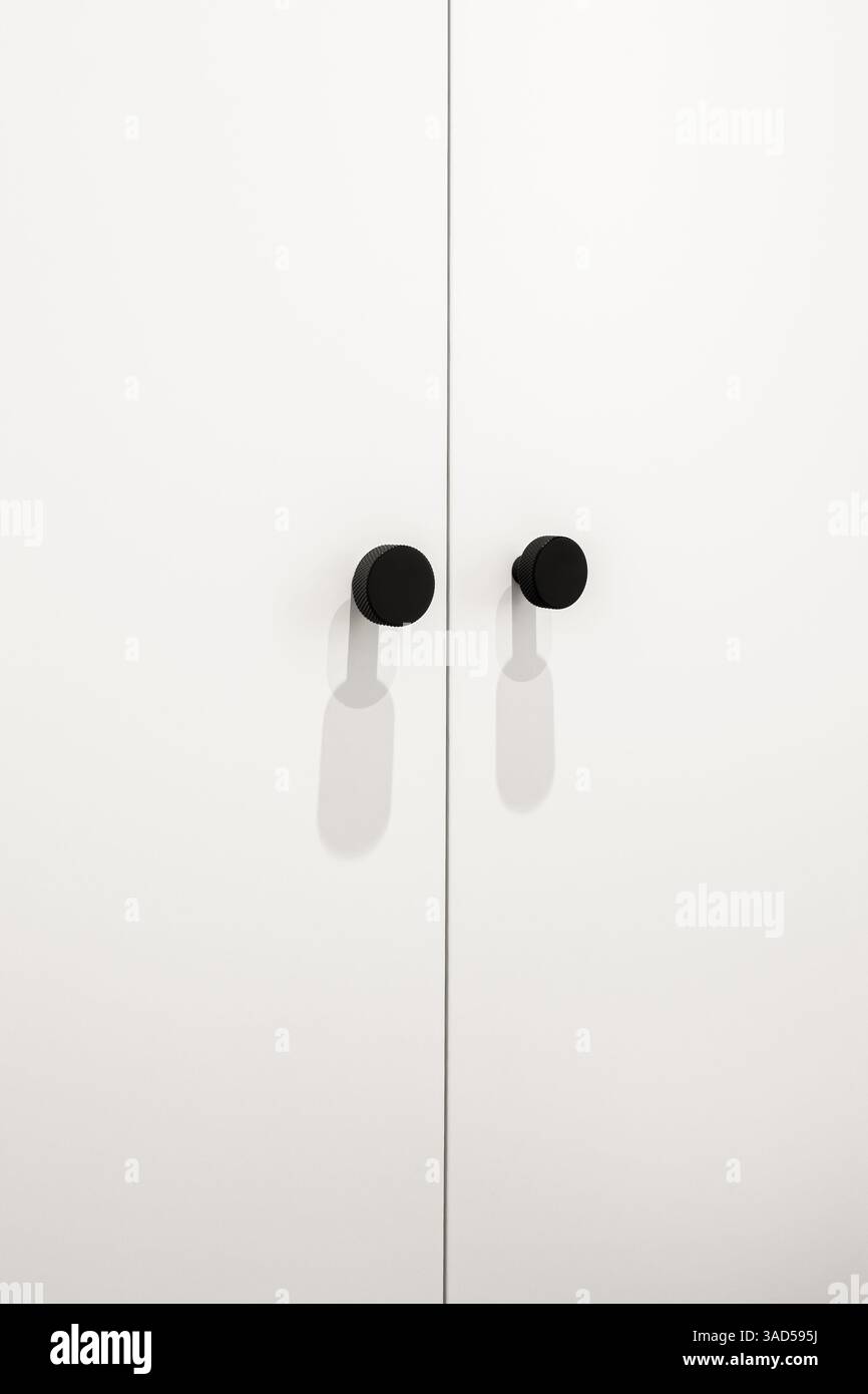 Symmetrische, moderne schwarze Griffe auf einem weißen Kleiderschrank mit sanfter Beleuchtung Stockfoto