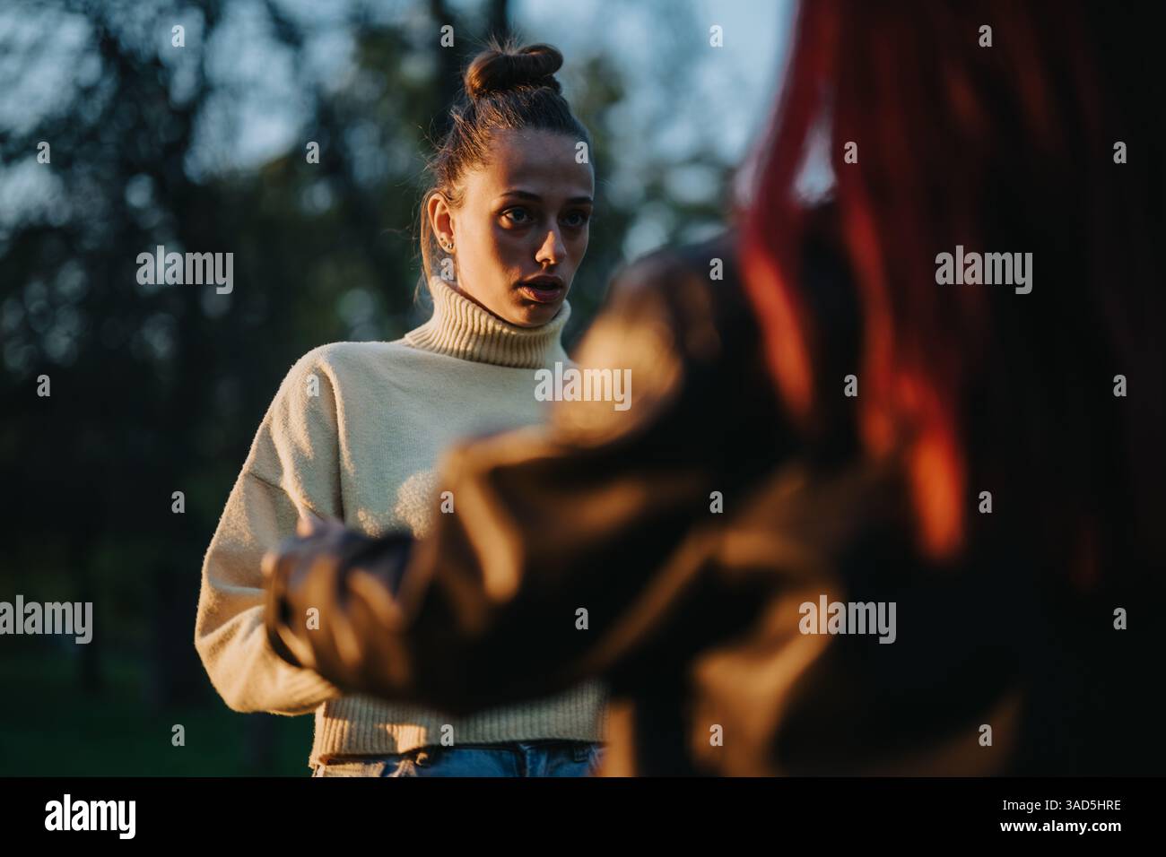 Zwei Frauen, die bei Sonnenuntergang im Freien interagieren, mit ernstem Ausdruck und natürlichem Licht Stockfoto