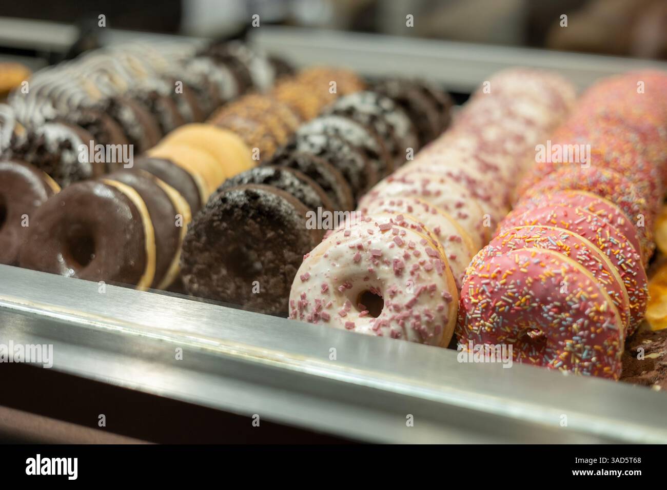 In einer Gebäckkiste werden Reihen von bunten und köstlichen Donuts präsentiert, die eine verlockende Auswahl an süßen Leckereien bieten. Stockfoto