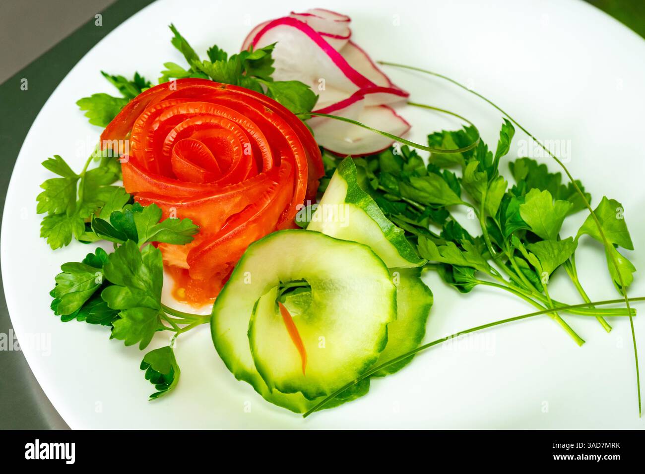 Wunderschön angeordnete Garnituren aus geschnittenen Tomaten, Gurken, Radieschen und frischen Kräutern werden auf einem weißen Teller präsentiert. Diese lebendige Vegeta-Show Stockfoto