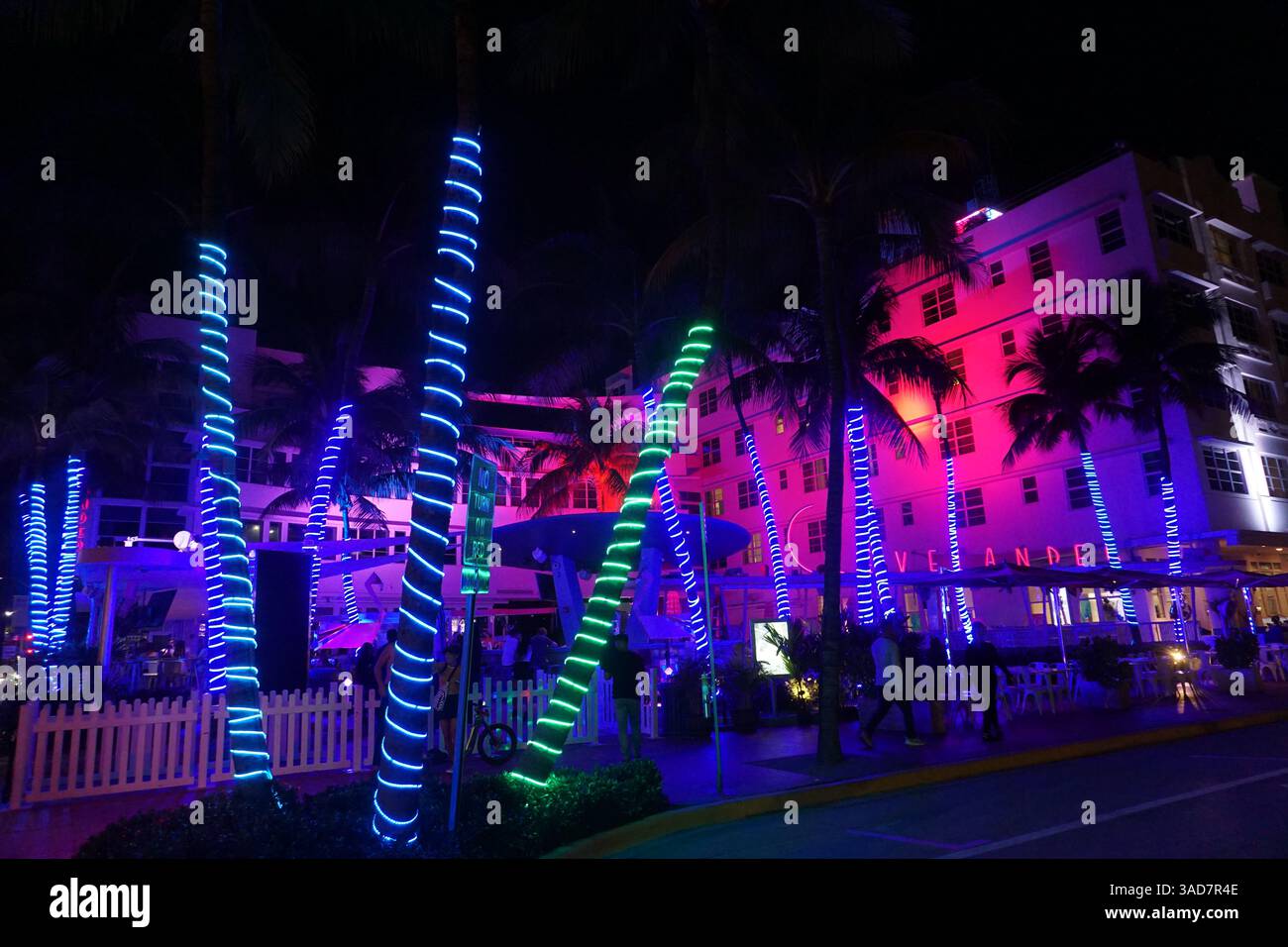 Touristen spazieren zwischen den Neonlichtern der beleuchteten Palmen auf einer Strandpromenade von Miami Beach/South Beach, um das Nachtleben in den Nachtclubs zu genießen. Stockfoto