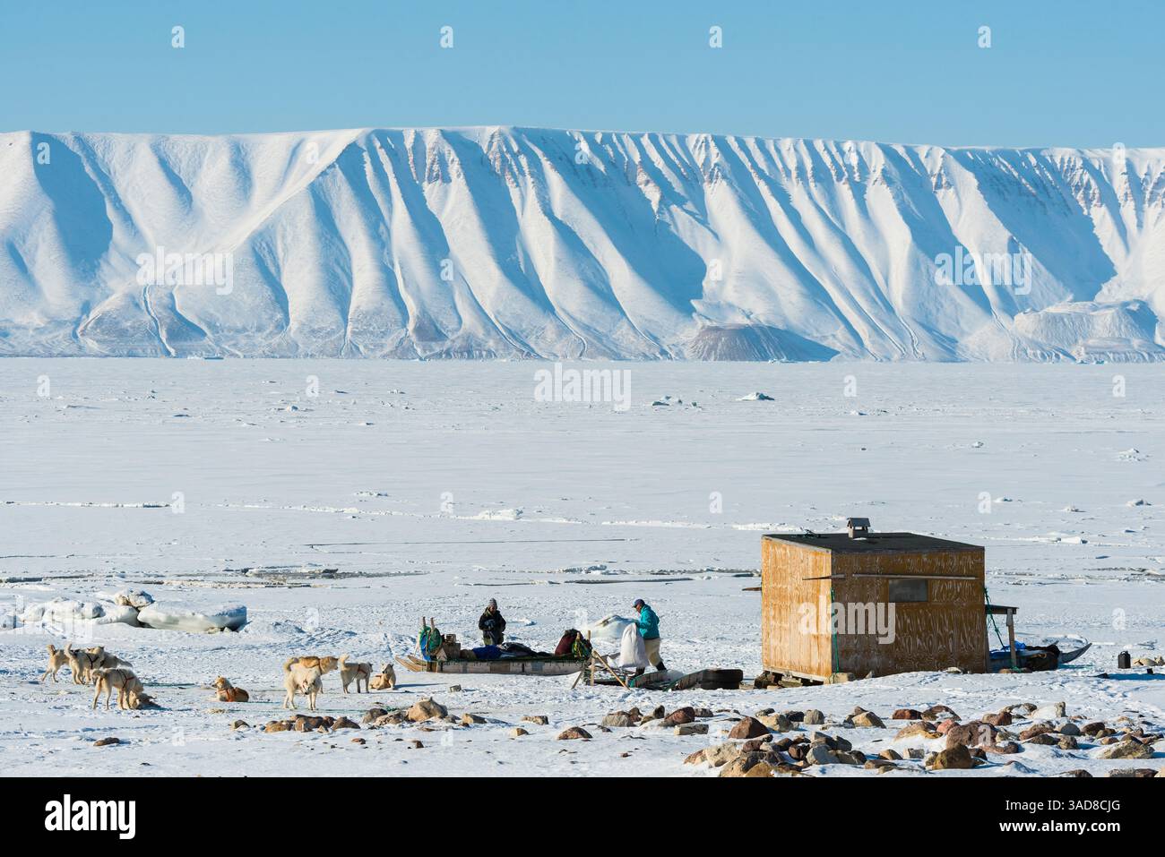 In einer abgelegenen Gegend von Camp Grönland nehmen zwei Personen Aktivitäten Teil, während sie von ausgedehntem, schneebedecktem Gelände und majestätischen Bergen umgeben sind. Wildlif Stockfoto
