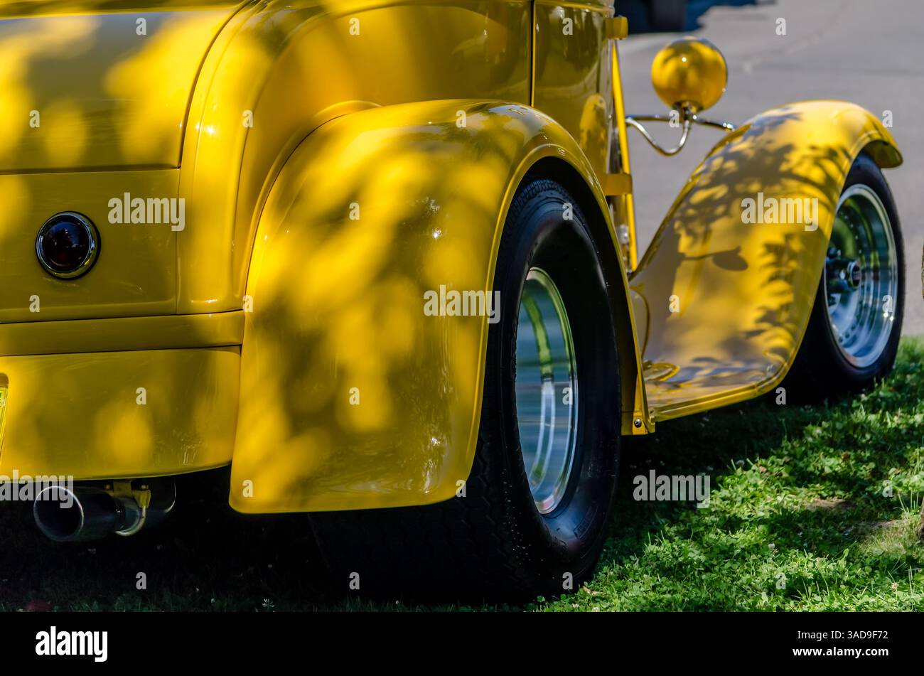 Nahaufnahme eines Dreiviertel-Rückfahrzeugs eines gelben Roadsters mit Trittbrett unter einem schattigen Baum Stockfoto
