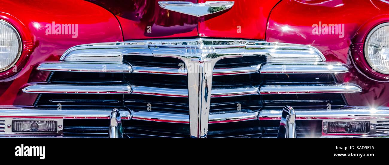Panoramablick auf den Grill eines Oldtimers und die rote Karosserie mit Sonnenflecken. Stockfoto