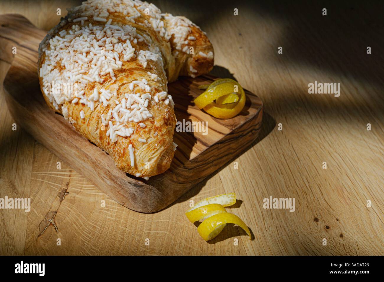 Zitronencroissant und Zitronenschale auf dem Holzbrett im Morgenlicht Stockfoto