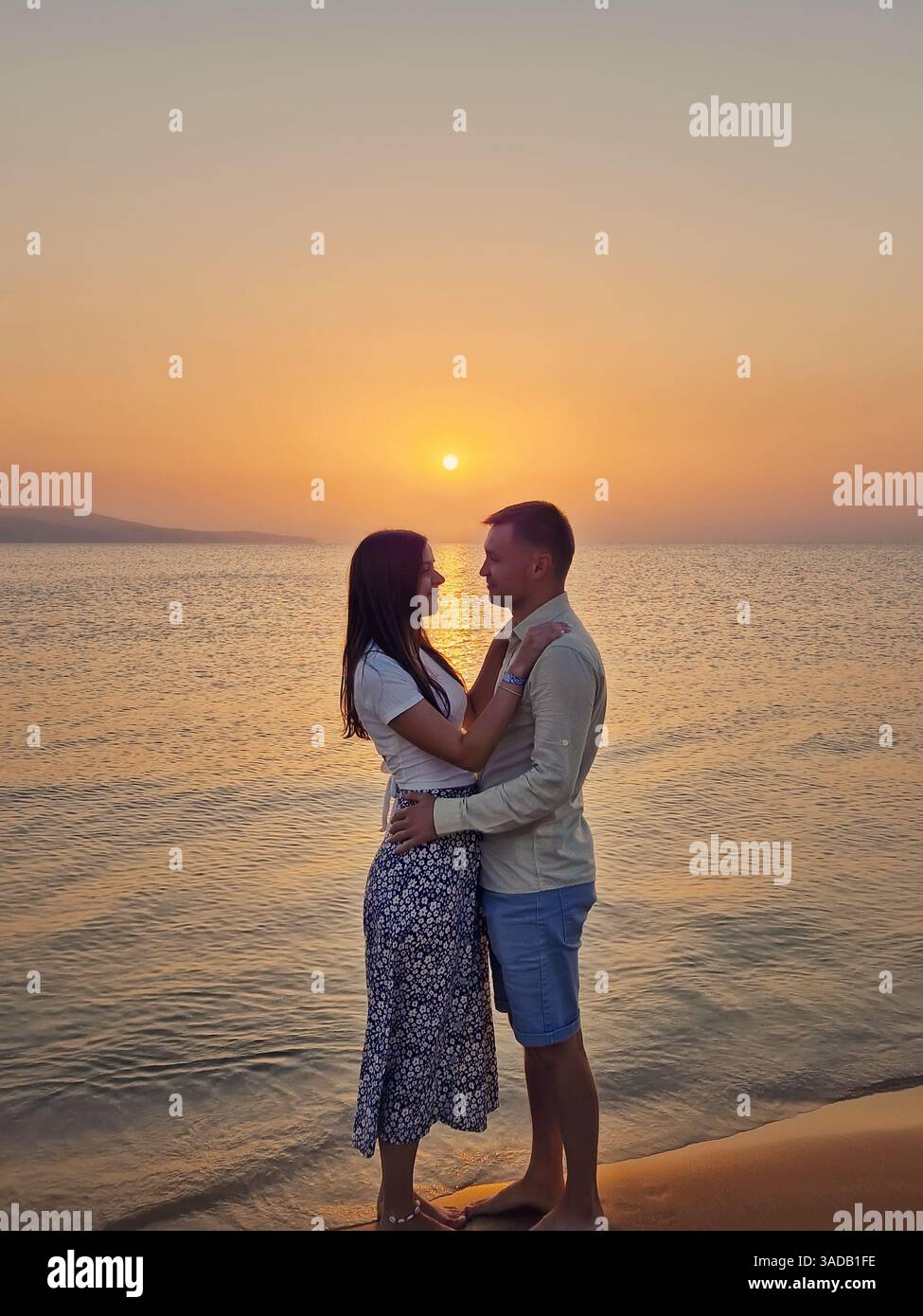 Ein junges Paar, das sich bei Sonnenaufgang an einem Date am Meer umarmt. Frau und Mann auf Hochzeitsreise treffen sich unten am Strand. Sommerurlaub, Liebe - Smartphone-aufgenommenes Stockfoto