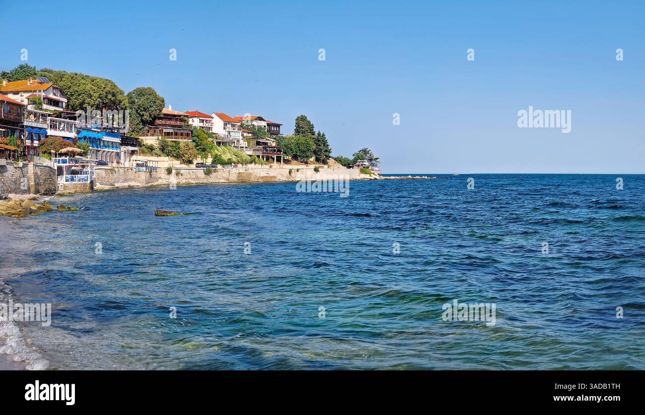 Ruhige Küstenszene mit klarem blauem Wasser und Kiesstrand und Gebäuden auf einem Hügel unter klarem Himmel. Die malerische Altstadt Nessebar - Smartphone-aufgenommenes Stockfoto