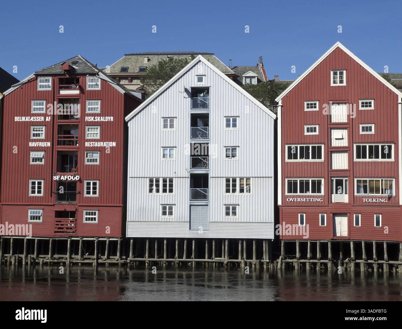 Rote Holzgebäude mit Restaurantschildern am Wasser, trondheim, norwegen, skandinavien Stockfoto