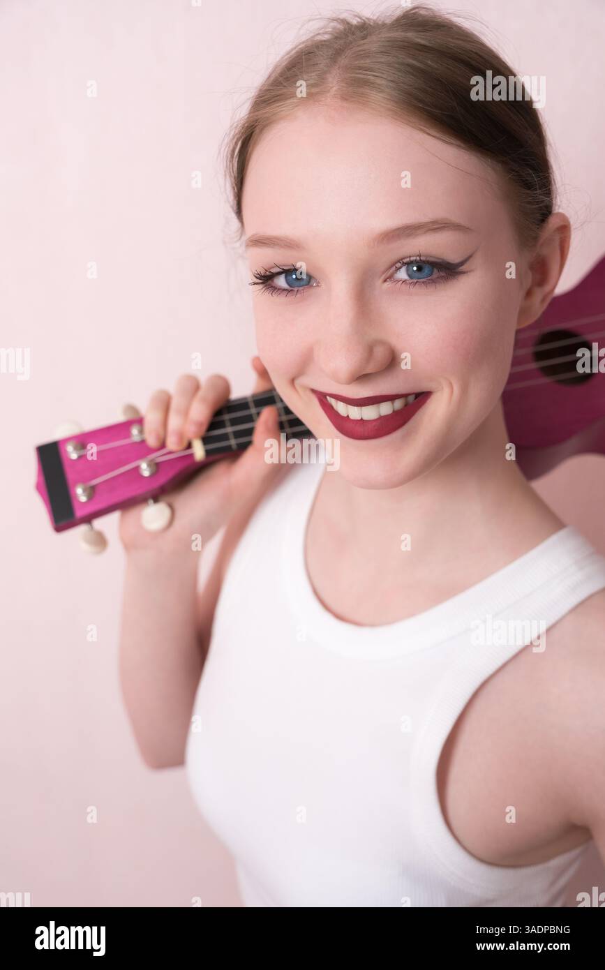 Eine junge Musikerin, die Ukulele am Hals hält und das Musikinstrument über die Schulter schleudert, sie fühlt sich inspiriert. Schöne Frau, die Kamera mit aussehender Kamera Stockfoto