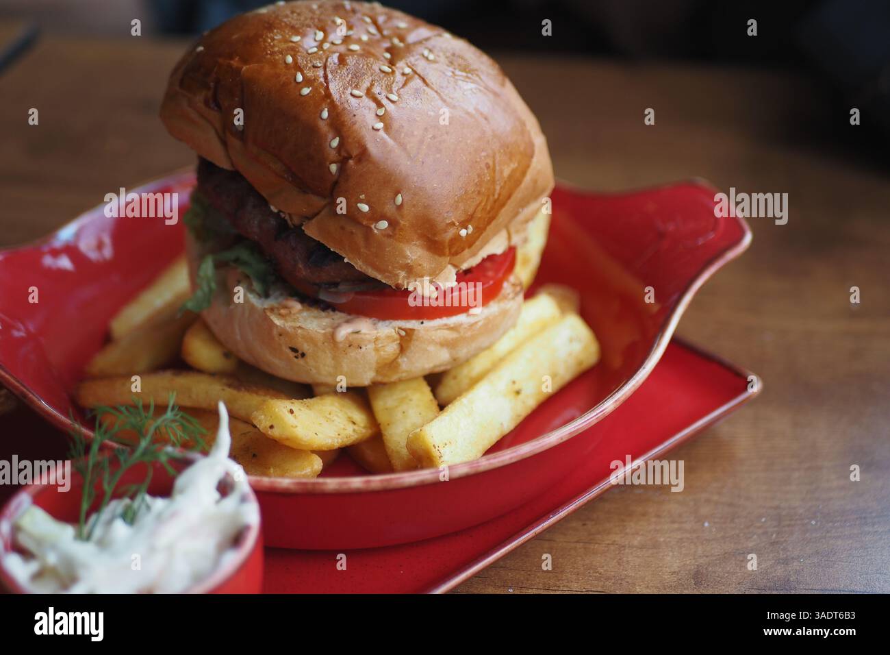 Köstlicher Hamburger mit Pommes frites, serviert auf einem lebhaften roten Teller Stockfoto