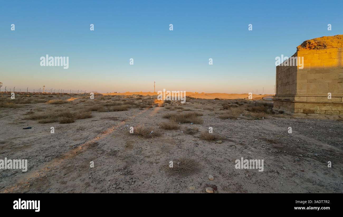 Eine riesige Wüstenlandschaft bei Sonnenuntergang mit einem klaren blauen Himmel und einer teilweise sichtbaren antiken Steinstruktur auf der rechten Seite. Stockfoto