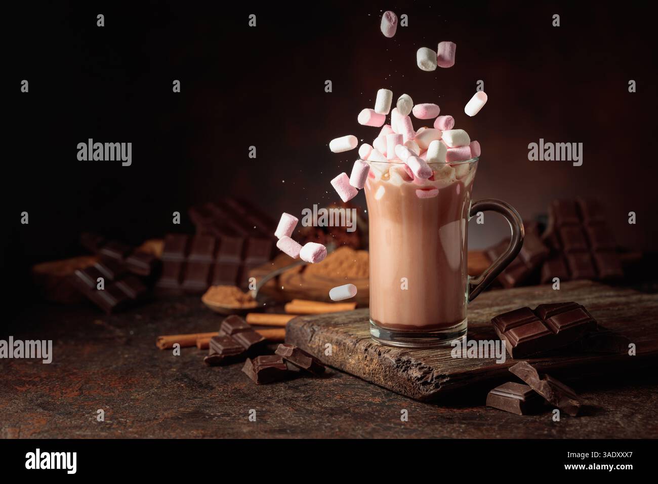 Marshmallows werden in einen Becher mit heißem Schokoladengetränk gegossen. Eine Tasse heiße Schokolade mit zerbrochenen dunklen Schokoladentafeln und Kakaopulver. Kopierbereich. Stockfoto