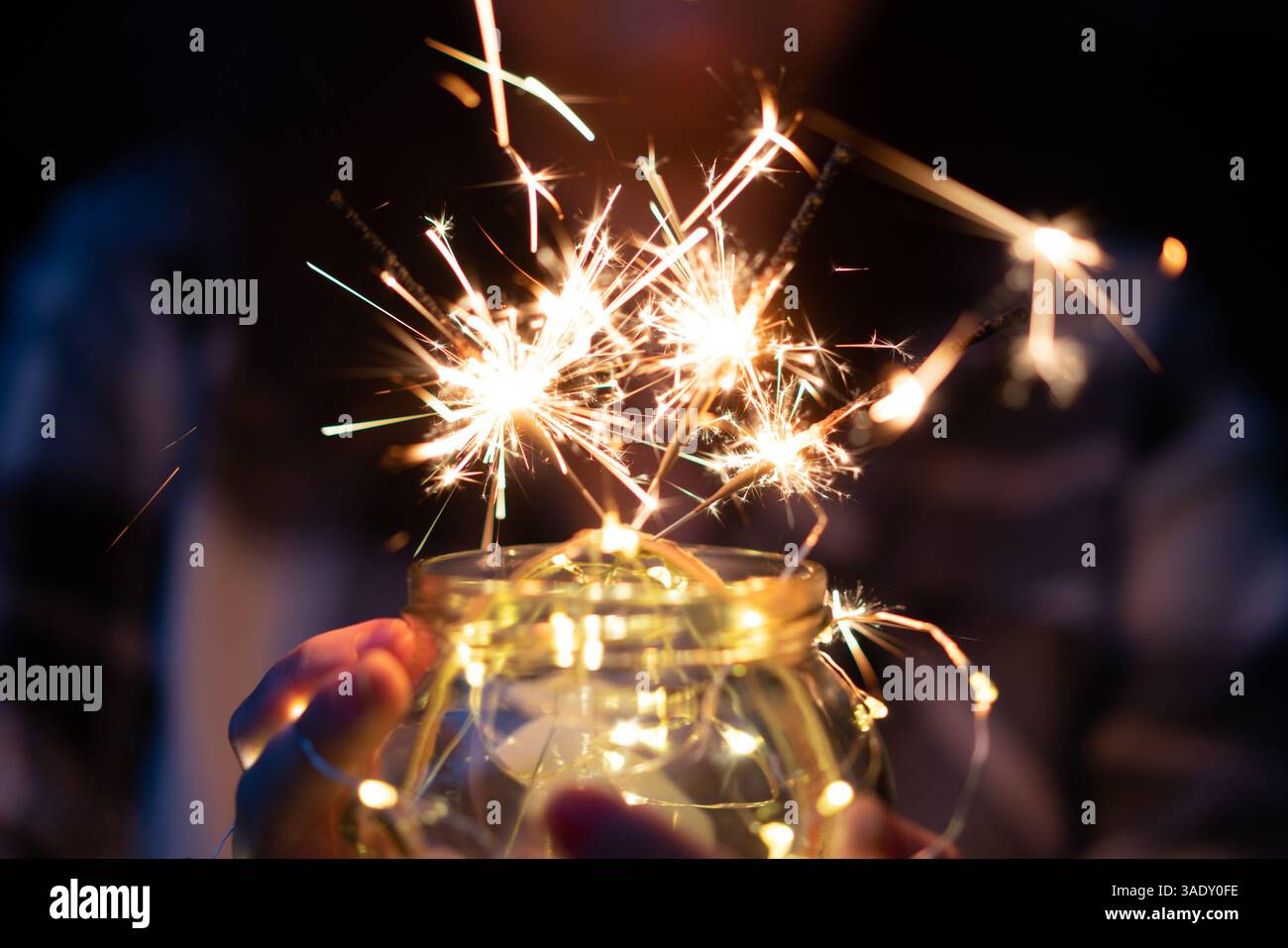 Wunderkerze in einem Glas in dunklem Hintergrund, gehalten von Händen einer Frau Stockfoto