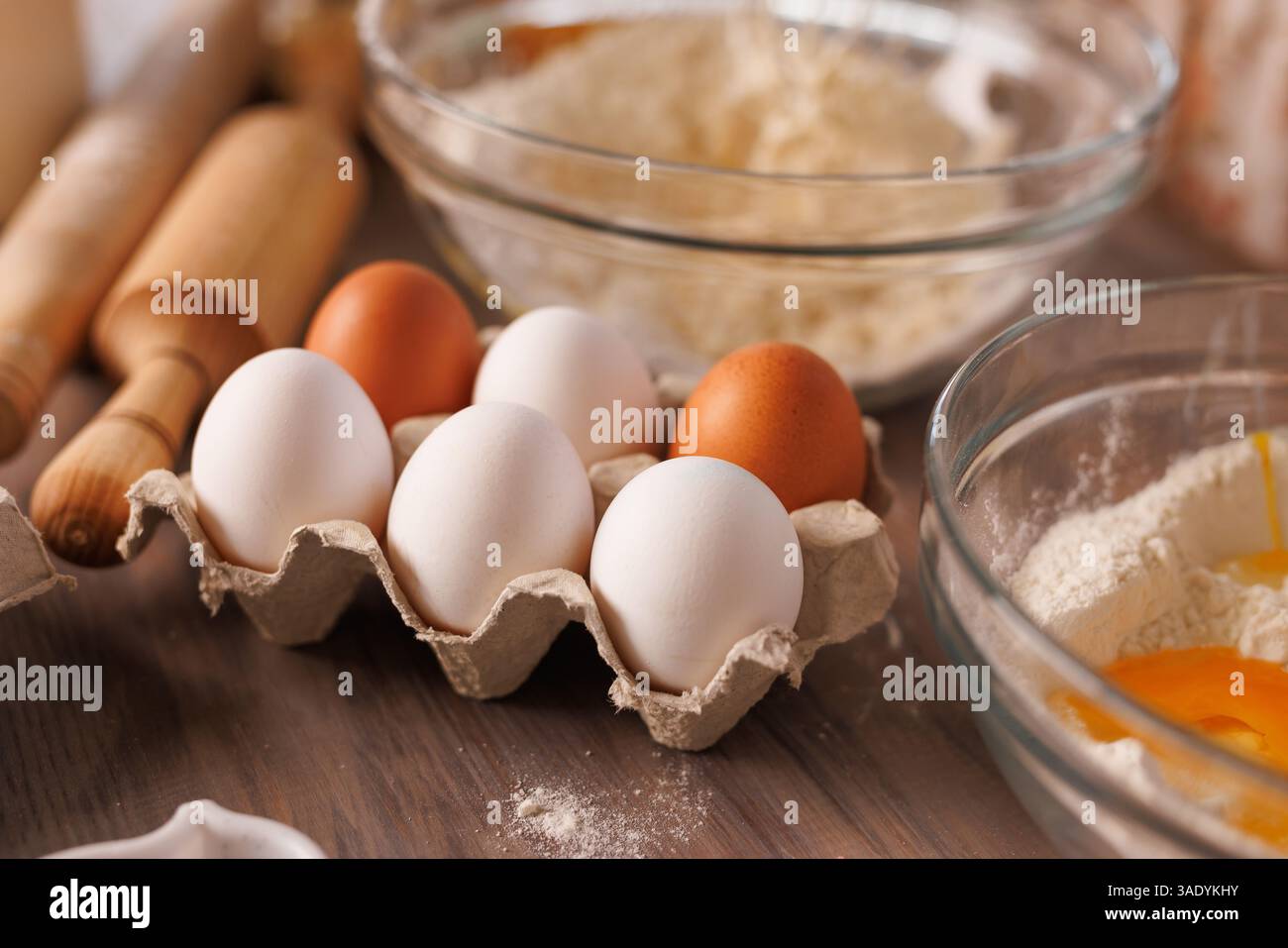 Frische Eier im Karton auf rustikaler Küchentheke mit Mehl und Nudelnadeln, Backzutaten zubereitet. Stockfoto