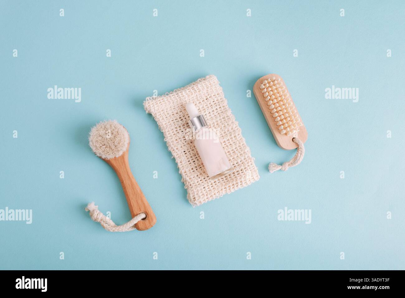 Hautpflege-Serum-Tropfflasche mit Bürsten und Schwamm auf blauem Hintergrund. Flache Lage, Draufsicht. Stockfoto