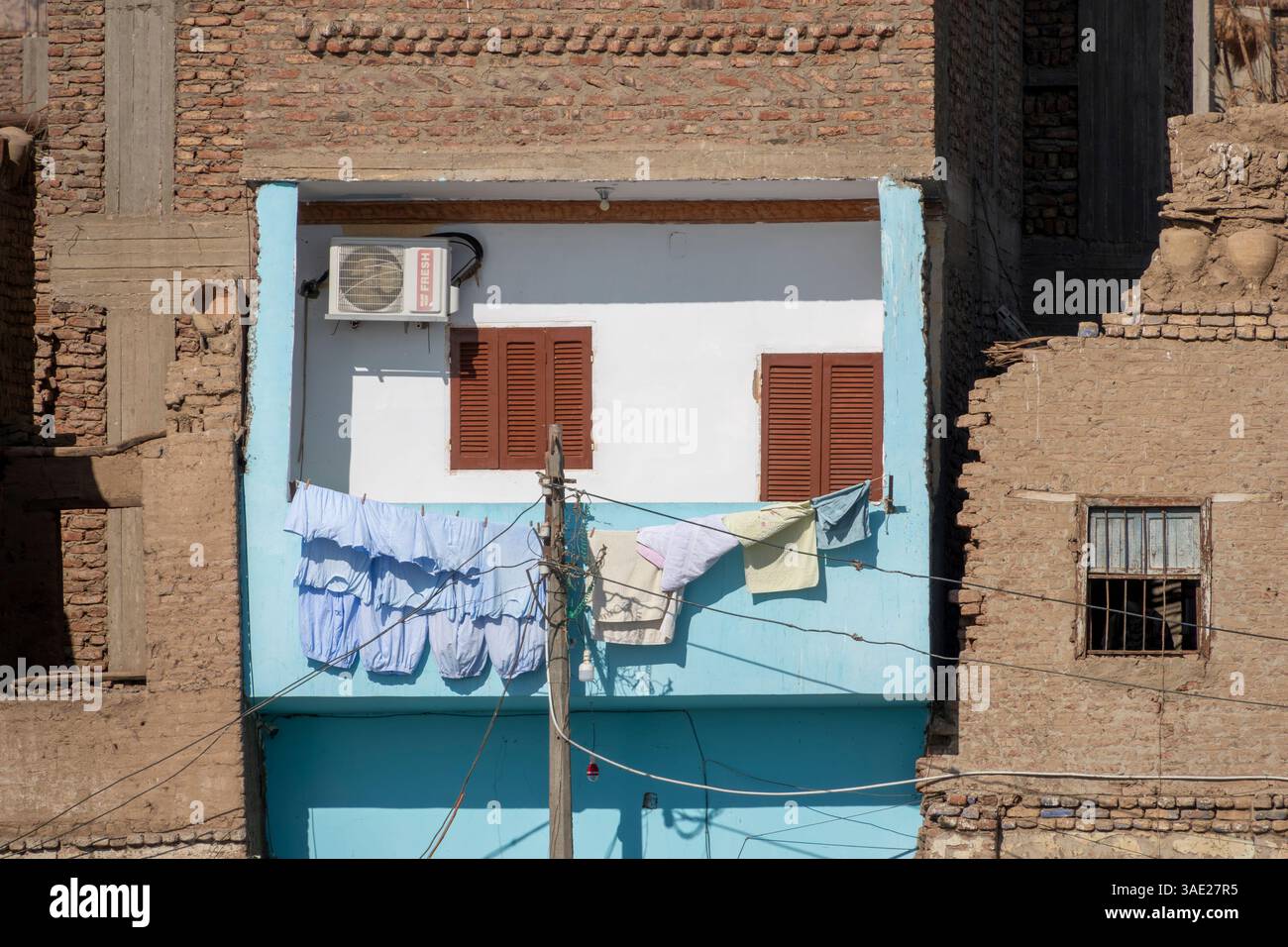 Ein Apartment-Balkon aus Ziegelstein und Beton, blau und weiß lackiert, mit Waschen, Trocknen in der Sonne, mit Fensterläden und Klimaanlage. Ägypten Stockfoto