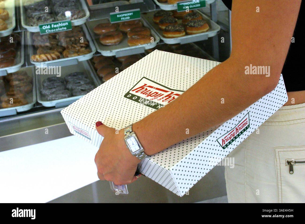 Oktober 2003; Laguna Niguel, CA, USA; Krispy Cream Donuts erobern die Welt im Sturm und die Leute scheinen nicht genug davon zu bekommen. Ein Kunde beobachtet die Produktion von zuckerbeschichteten Donuts, wie sie in jedem Krispy Kream-Geschäft zu sehen ist, während er ein Dutzend glasierte Donuts kauft. Sie haben mittlerweile über 300 Filialen weltweit. (Bild: Ruaridh Stewart/ZUMAPRESS.com) Stockfoto