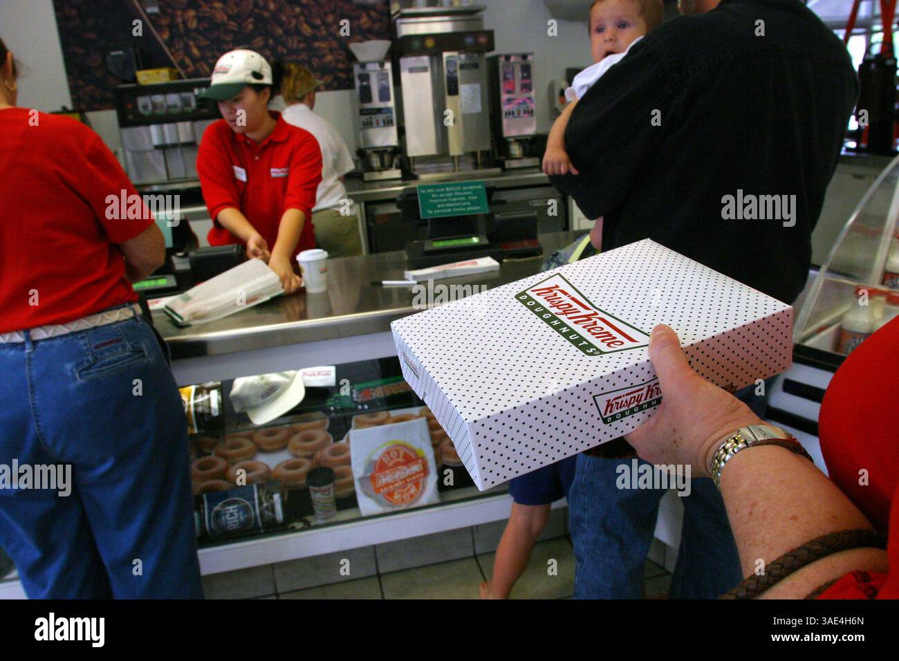 Oktober 2003; Laguna Niguel, CA, USA; Krispy Cream Donuts erobern die Welt im Sturm und die Leute scheinen nicht genug davon zu bekommen. Ein Kunde beobachtet die Produktion von zuckerbeschichteten Donuts, wie sie in jedem Krispy Kream-Geschäft zu sehen ist, während er ein Dutzend glasierte Donuts kauft. Sie haben mittlerweile über 300 Filialen weltweit. (Bild: Ruaridh Stewart/ZUMAPRESS.com) Stockfoto