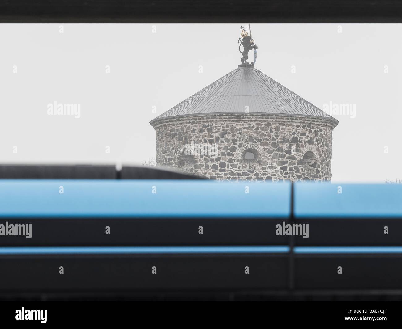 An einem nebeligen Tag in Göteborg fährt ein blauer Bus am historischen Skansen Lejonet vorbei. Der berühmte Steinturm ist teilweise von Nebel verdeckt und der Bus fügt hinzu Stockfoto