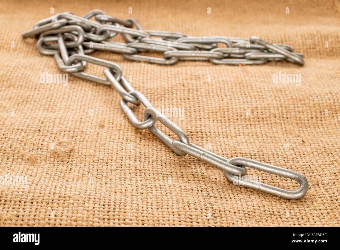 Ein Stück Metallkette auf Jute-Tuch, Makro. Stockfoto