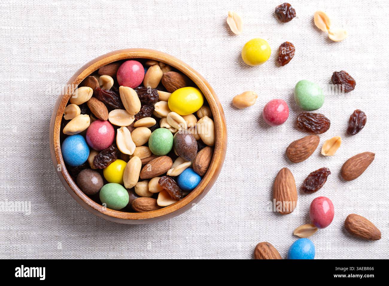 Rainbow Trail Mix in einer Holzschale auf Leinenstoff. Eine Snackmischung aus Erdnüssen aus Milchschokolade, gerösteten Erdnüssen, Rosinen und gerösteten Mandeln. Stockfoto