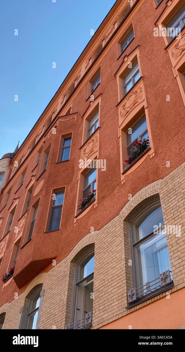 Fassade eines historischen europäischen Gebäudes mit kunstvollen architektonischen Details, Blumenkästen und strukturierten orangen Wänden unter klarem blauen Himmel. - Smartphone-aufgenommenes Stockfoto