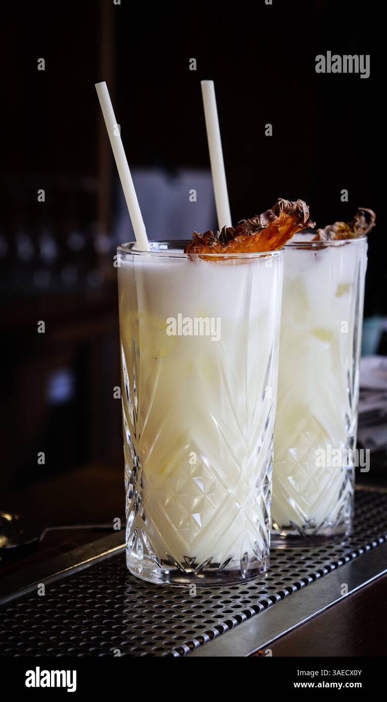Cremige, saure Ananascocktails an einer typischen Bartheke, dekoriert mit einer Ananasscheibe und einem weißen Strohhalm Stockfoto