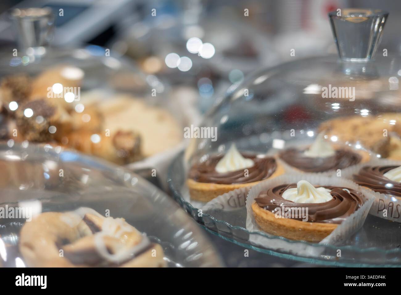 Gebäck unter Glaskuppeln auf einer Ausstellungstheke, einschließlich Schokoladentörtchen. Stockfoto