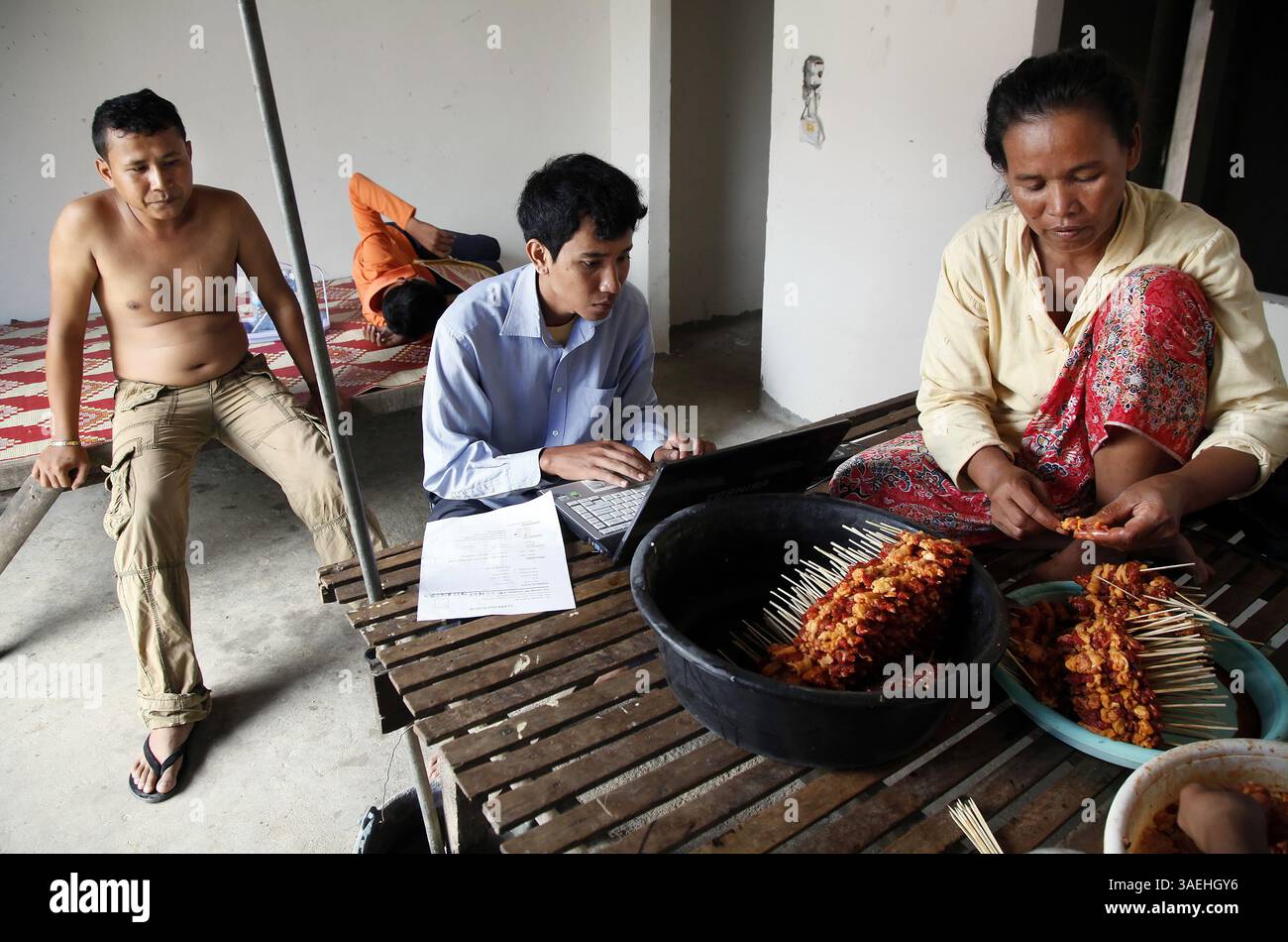 4. Oktober 2011 - Phnom Penh, KHM - im Zentrum hilft Chhum Bunthy, 25, seinem Nachbarn Ngeth Vannak, auf der linken Seite bereitet er seinen Lebenslauf vor, während seine Mutter Chun Chhen am 4. Oktober 2011 in ihrem Haus in Phnom Penh, Kambodscha, Fleisch für den Verkauf auf der Straße zubereitet. Bunthy studiert Architektur an der Norton University in Phnom Penh und erhält ein Stipendium von Digital Divide Data (DDD), das 60 Prozent seiner Studiengebühren bereitstellt. (Kreditbild: © Lipo Ching/San Jose Mercury News/MCT/ZUMAPRESS.com) Stockfoto 4. Oktober 2011 - Phnom Penh, KHM - im Zentrum hilft Chhum Bunthy, 25, seinem Nachbarn Ngeth Vannak, auf der linken Seite bereitet er seinen Lebenslauf vor, während seine Mutter Chun Chhen am 4. Oktober 2011 in ihrem Haus in Phnom Penh, Kambodscha, Fleisch für den Verkauf auf der Straße zubereitet. Bunthy studiert Architektur an der Norton University in Phnom Penh und erhält ein Stipendium von Digital Divide Data (DDD), das 60 Prozent seiner Studiengebühren bereitstellt. (Kreditbild: © Lipo Ching/San Jose Mercury News/MCT/ZUMAPRESS.com) Stockfoto