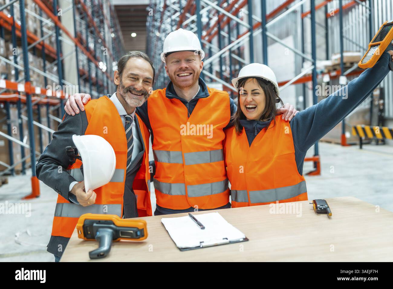 Lagerarbeiter und ihre Manager umarmen sich gegenseitig und feiern einen erfolgreichen Logistikbetrieb in einem großen Vertriebszentrum Stockfoto