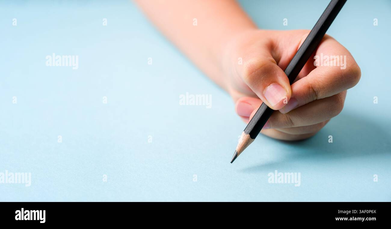 Die linke Hand hält einen Kugelschreiber auf einem offenen Notizbuch auf blauem Hintergrund Stockfoto