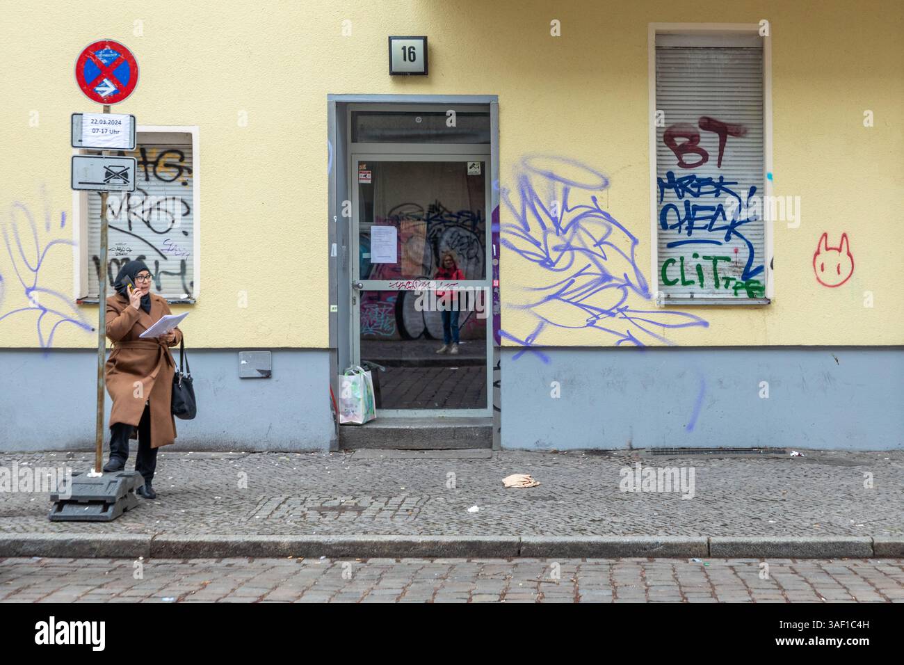 Berlin, Deutschland - 22. März 2024: Frau mit lustiger Mütze, die das Handy benutzt, während sie auf Abholung in berlin Neukölln wartet, typisches Straßenleben für diesen Ar Stockfoto