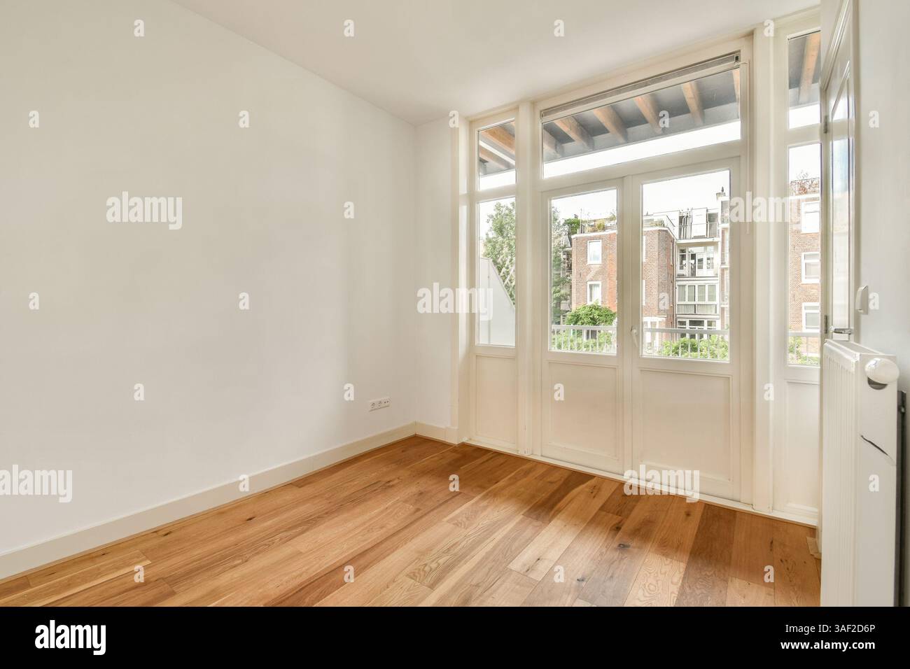 Ein geräumiger und minimalistischer Raum mit großen Fenstern, die natürliches Licht einlassen, mit Holzboden und neutralen Wänden, ideal für modernes Wohnen. Stockfoto