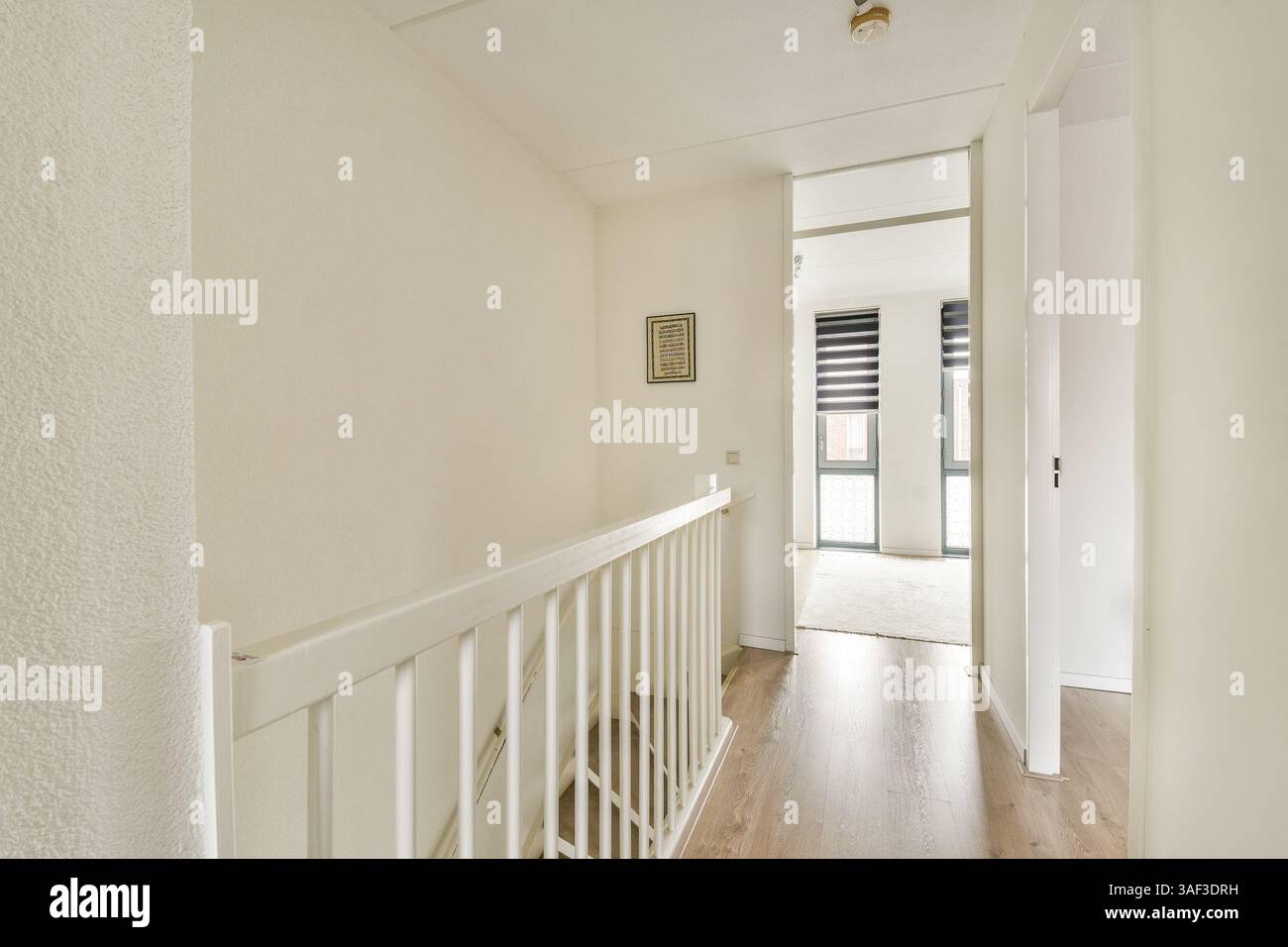 Dieses Bild zeigt einen hellen und modernen Flur mit weißen Wänden und Holzböden, der zu einem geräumigen Bereich führt. Tageslicht durchflutet große Fenster. Stockfoto