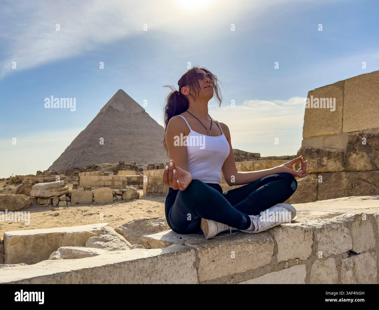 Erleben Sie eine Frau, die zwischen den Pyramiden von Gizeh Yoga praktiziert und sich mit Mycerinus, Kefren und Keops verbindet. Erleben Sie die spirituelle Verbindung in dieser Anstiftung Stockfoto