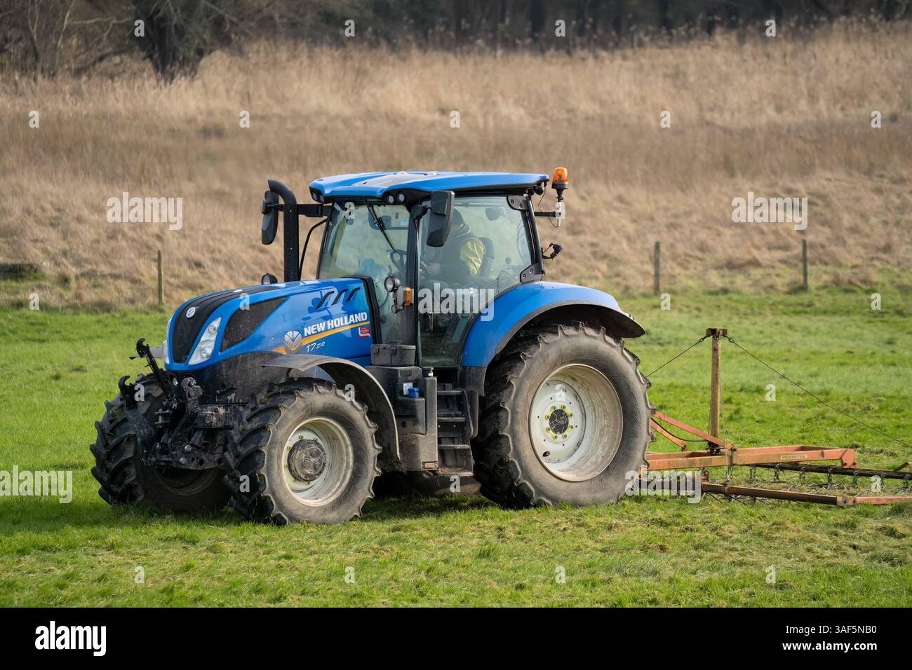 New Holland T7 225 Traktor zieht eine Egge über eine Wiese Stockfoto
