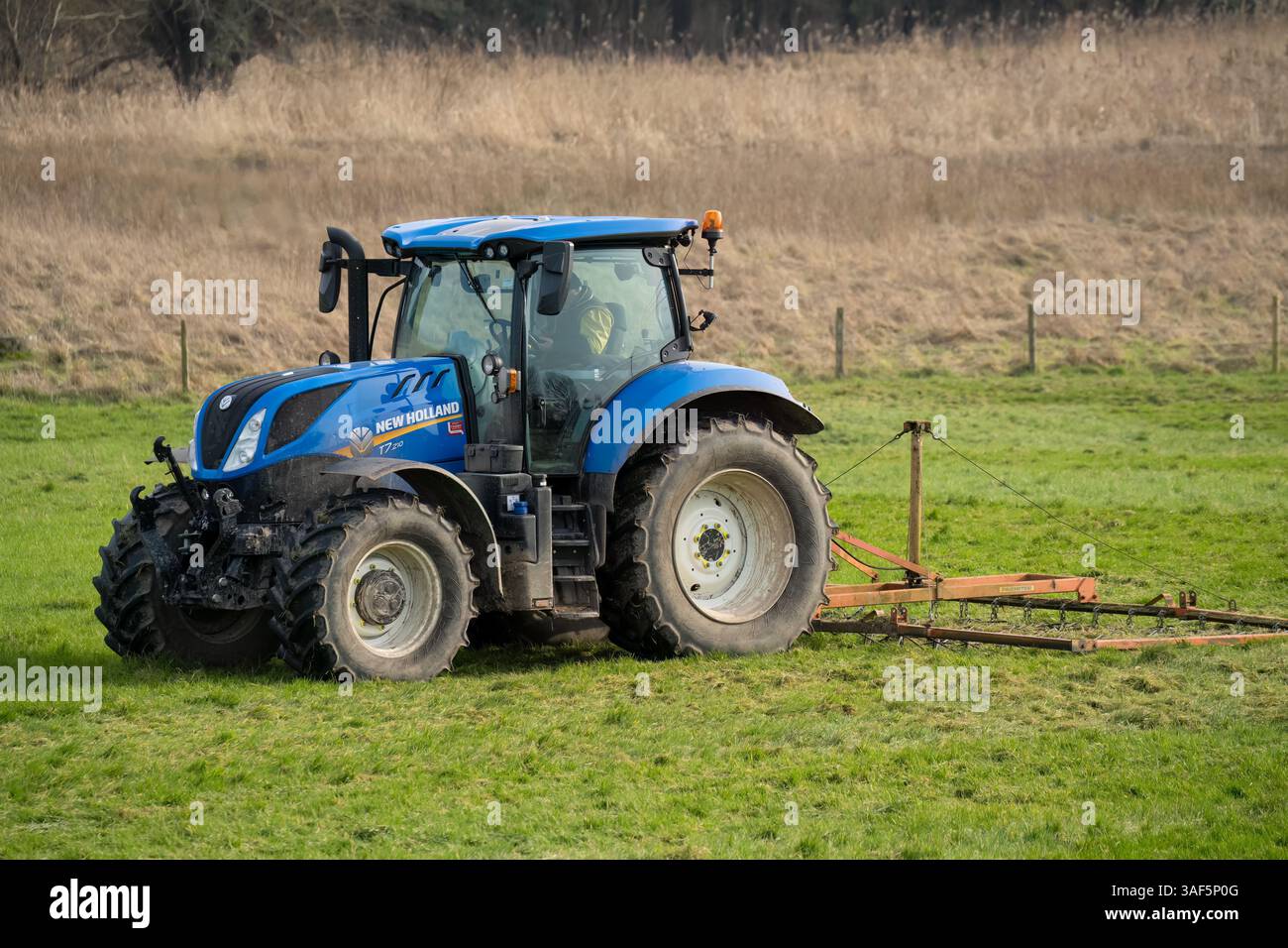 New Holland T7 225 Traktor zieht eine Egge über eine Wiese Stockfoto