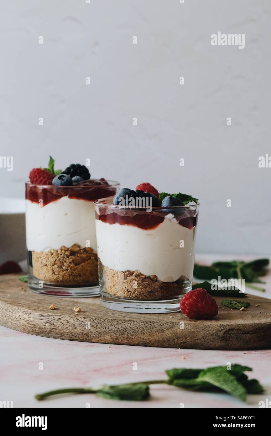 Kleinigkeiten, Parfait oder Käsekuchen auf Gläsern, Schichten Crumble Cookies, weiße Creme, Erdbeermarmelade und Beeren auf Minzblättern. Stockfoto