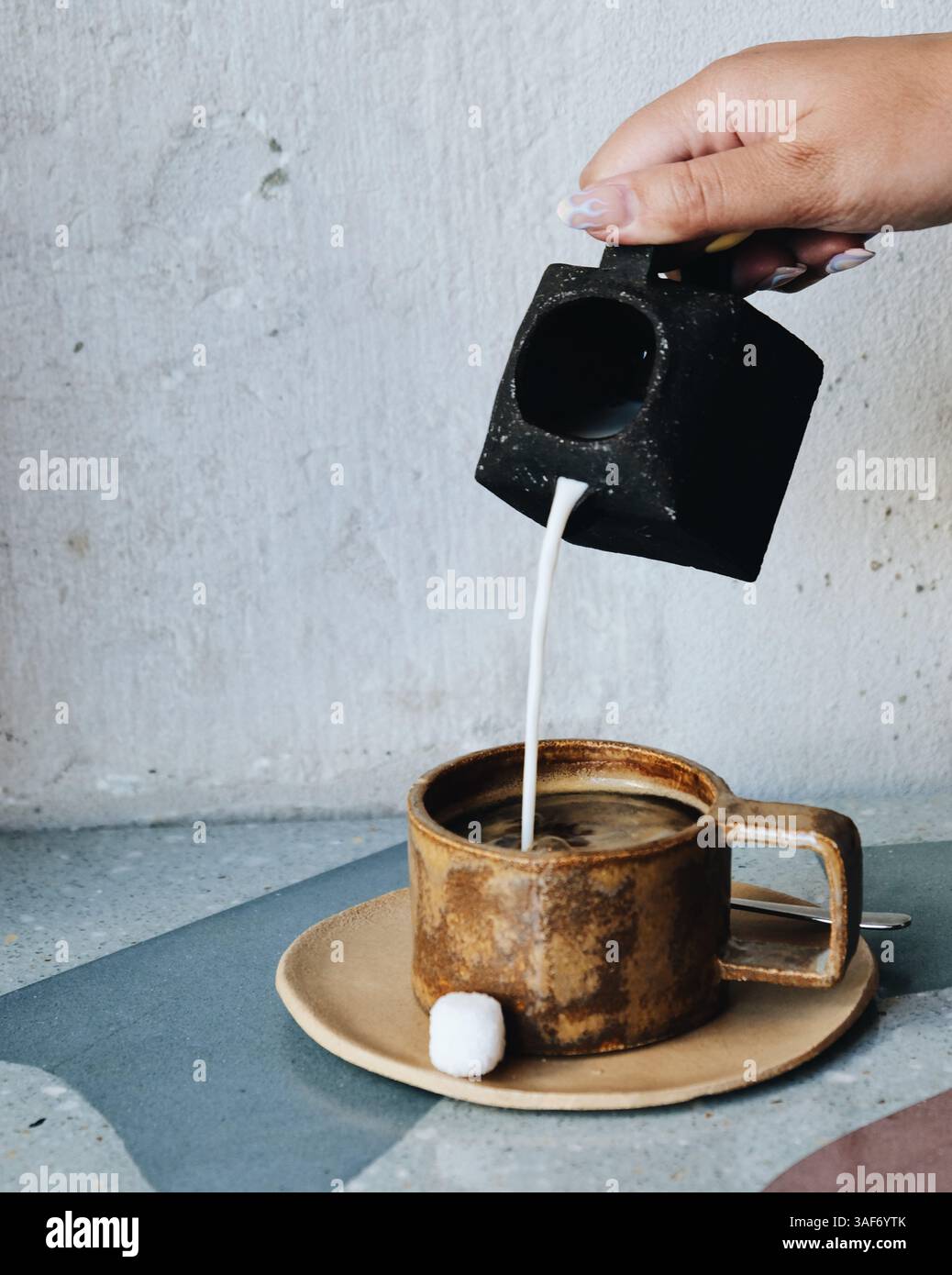 Tasse Kaffee, Becher und Teller auf brauner, moderner Keramik, Zuckerwürfel und eine Tasse Milch darüber. Blauer und grauer Hintergrund, saubere Ästhetik Stockfoto