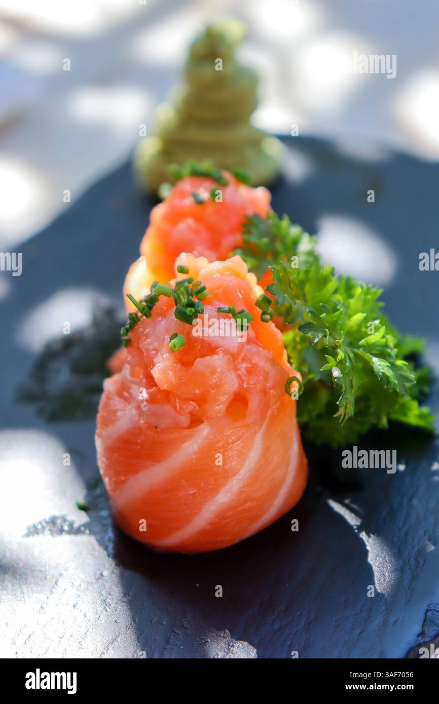 Lachs-Sushi-Maki-Rollen, dekoriert mit Kräutern und Wasabi, auf einem flachen dunklen Teller oder Tablett, auf weißem Hintergrund. Sommerlicht, Schatten. Mittagsstimmung oder earl Stockfoto