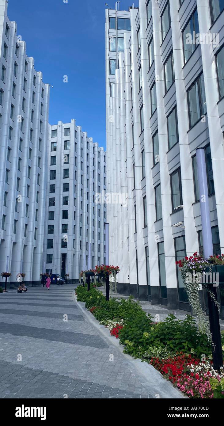 Moderne Bürogebäude mit vertikalen Linien und Blumenbeeten in einer Fußgängerzone. Städtische Architektur, Symmetrie und sauberes Design in einem Unternehmen Stockfoto