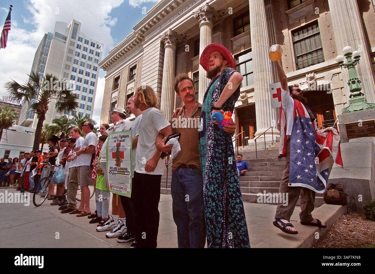 TP.103397.- LIEFERUNG AN:.Floridian.- 6.5.2000.- Tampa.- BILDUNTERSCHRIFT INFO:. Foto 3) Moe St. Evergreen (cq) (in Kleid und Hut), aus Tampa, singt gemeinsam mit anderen, die Give Peace A Chance (Give Peace A Chance) in einer Solidaritätsbekundung, nachdem Polizeibeamte aus Tampa am Samstagnachmittag mehrere Männer wegen Drogenkonsums vor dem Bundesgericht in Tampa verhafteten. Der Mann mit der Flagge identifizierte sich mit dem Namen Hairy Jesus und hielt den Gallonenkrug (Credit Image: St Petersburg Times/ZUMAPRESS.com) Stockfoto