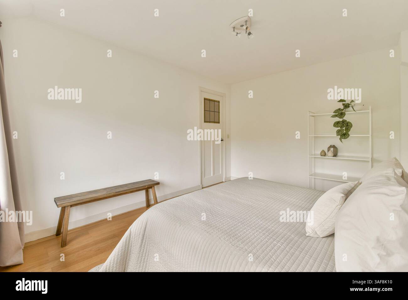 Ein ruhiges, minimalistisches Schlafzimmer mit hellen Wänden, natürlichem Holzfußboden und einem einfachen Bett, das Ruhe und Entspannung fördert. Stockfoto