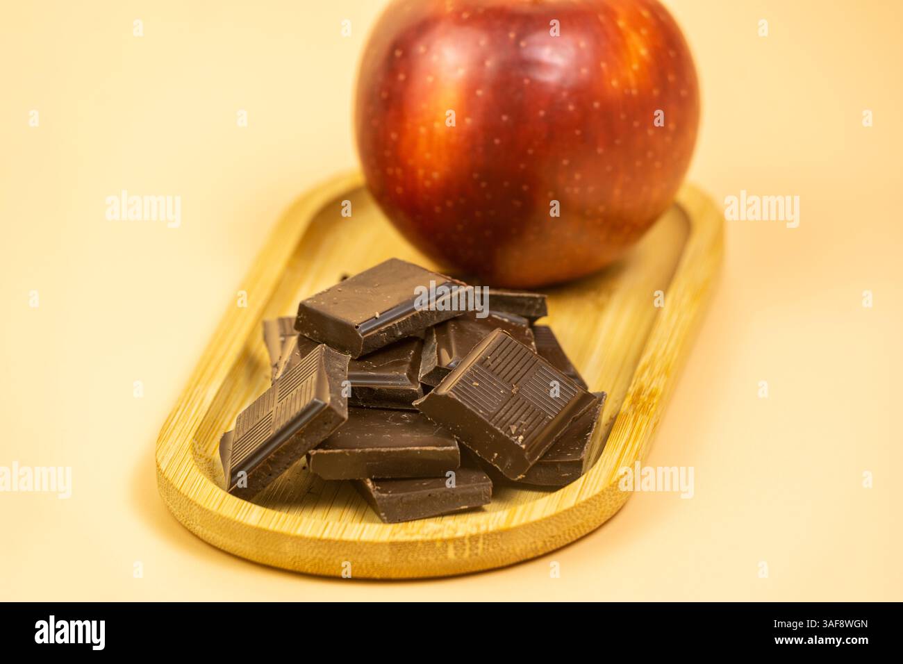 Kleines Bambustablett mit Schokoladenstückchen und einem Apfel auf cremefarbenem Hintergrund Stockfoto Kleines Bambustablett mit Schokoladenstückchen und einem Apfel auf cremefarbenem Hintergrund Stockfoto