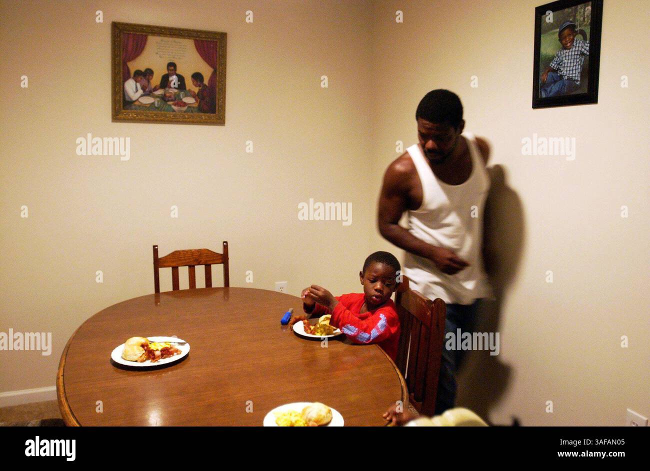 27.08.05, Charlotte) FOTO 3: Ernest Henard (CQ-Reporter) bringt Frühstück, als sein Sohn Nathan (CQ), 4, widerwillig versucht, auf alle zu warten, die am Tisch sitzen, bevor er mit dem Essen beginnt. Die Henards leben in einer erschwinglichen Mietwohnung, die während der zweiten Phase der First Ward Mixed-Income-Entwicklung in Charlotte, North Carolina, gebaut wurde. Henard ist auf Arbeitslosigkeit, seine Frau ist Lehrerin. ZUSAMMENFASSUNG: Vor zehn Jahren war Earle Village in Charlotte, North Carolina ein heruntergekommenes, drogenbefallenes Regierungsprojekt. Die Charlotte Housing Authority erhielt einen Zuschuss zur Revitalisierung von 1,6 Millionen HUD Stockfoto
