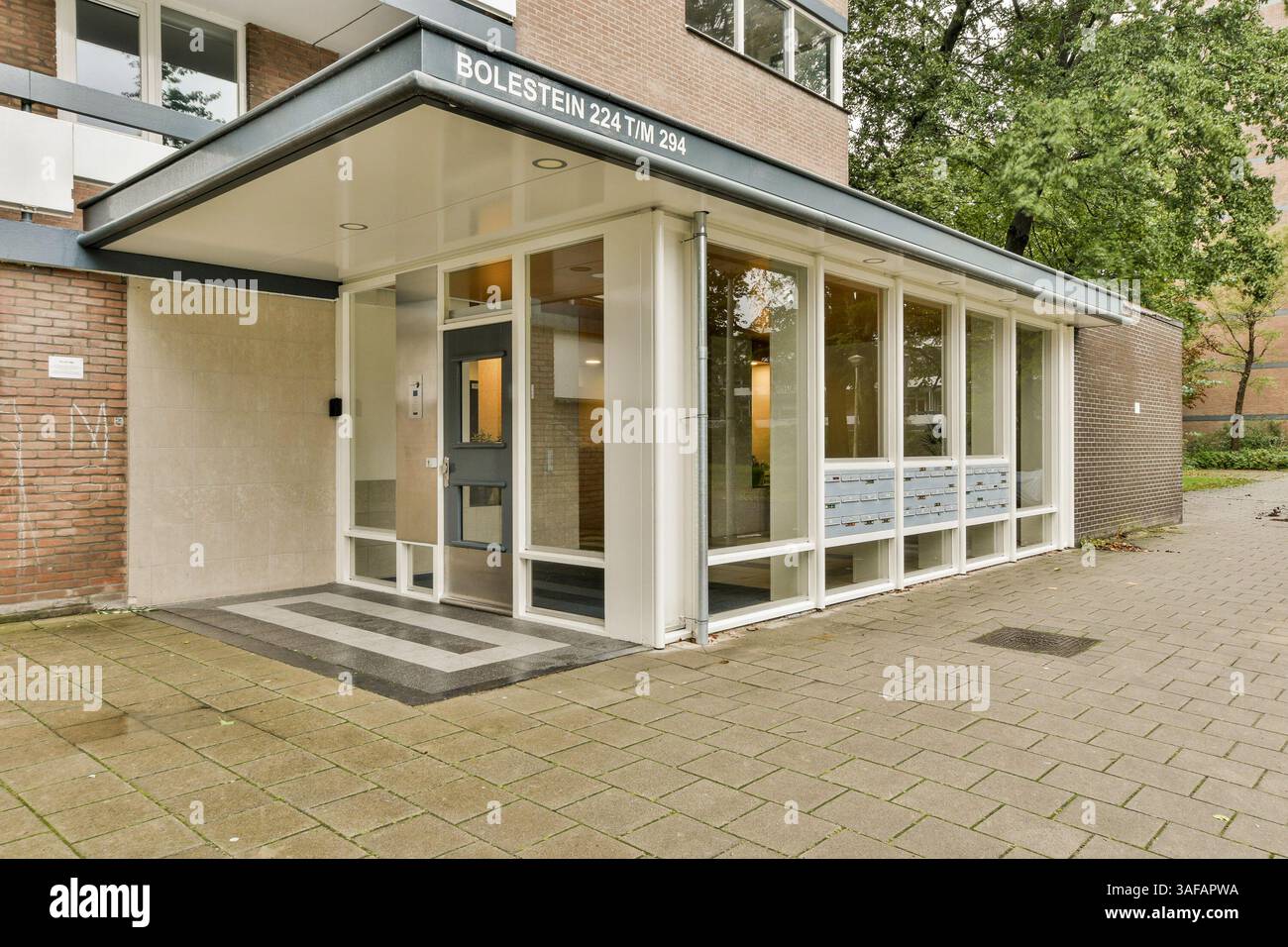 Ein moderner Eingang mit großen Glastüren und elegantem Design, umgeben von Grün. Das Gebäude verbindet moderne Architektur mit funktionaler Ästhetik. Stockfoto