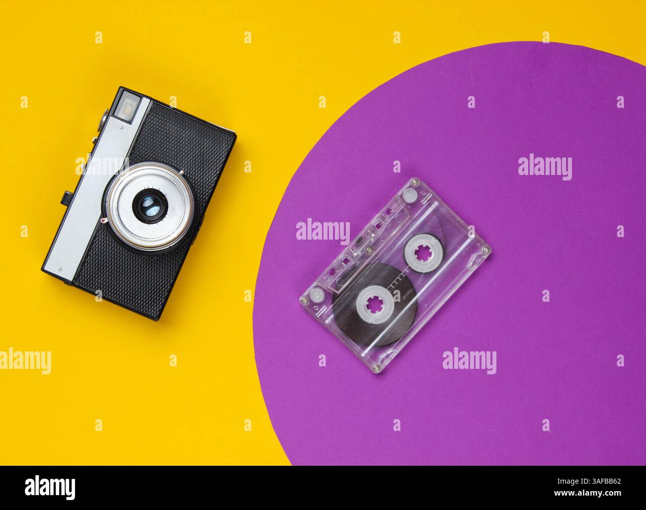Audiokassette und Retro-Filmkamera auf gelbem Hintergrund mit violettem Kreis. Modeschöpfung im Studio. 80er Jahre, Popkultur. Draufsicht. Stockfoto