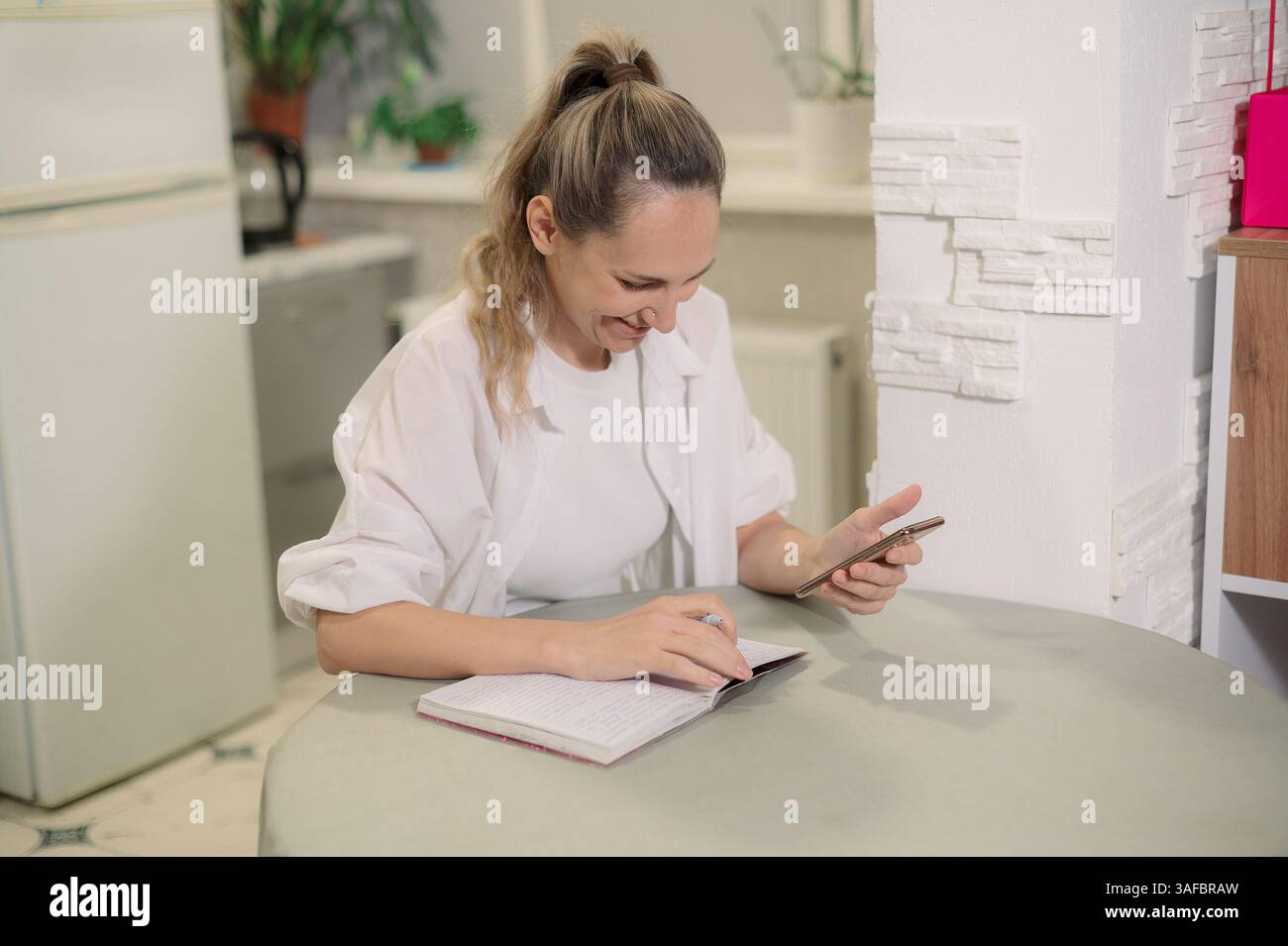 Zuhause mit einer Hand, die den Kalender des Smartphones überprüft und auf der Agenda t bei Frau schreibt Stockfoto