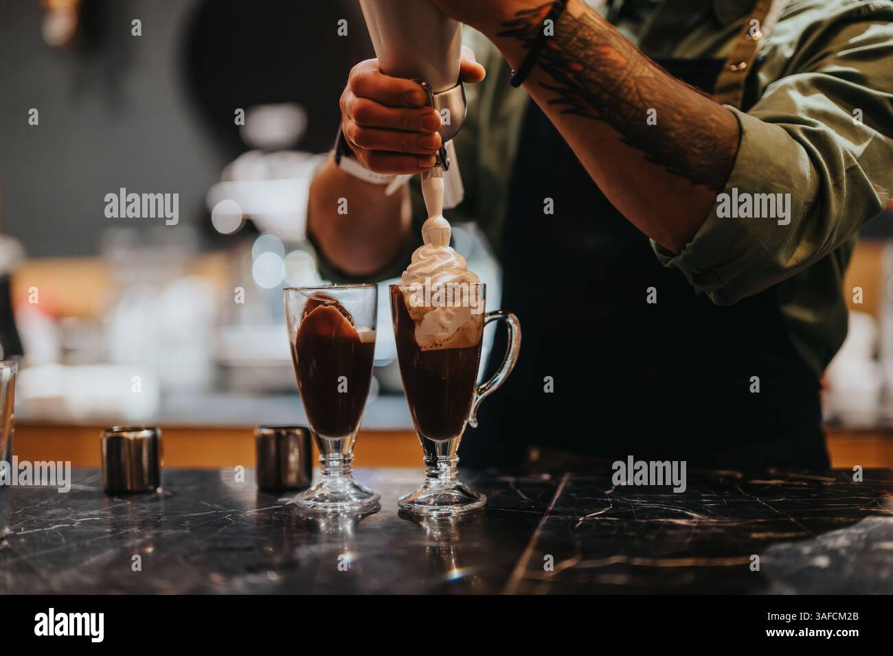 Barista bereitet heiße Schokolade mit Schlagsahne in Glasbechern zu Stockfoto