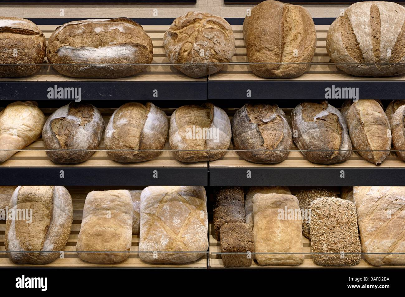 Verschiedene Arten von traditionellem hausgemachtem Brot auf den Holzregalen eines Bäckereigeschäfts, abstrakter Backwarenhintergrund Stockfoto
